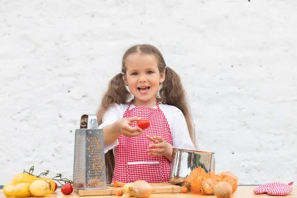 Happy little girl in an  chef costume helps to cook a pie by kneading the dough, a child smiles, cooking according to a recipe, a girl helps to cook for mom, a child\'s portrait and development.