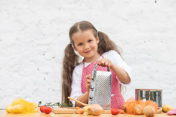 Happy little girl in an  chef costume helps to cook a pie by kneading the dough, a child smiles, cooking according to a recipe, a girl helps to cook for mom, a child\'s portrait and development.