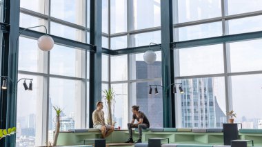 İki beyefendi, gökdelenlerin arka planında bir binanın tepesindeki ortak çalışma alanında toplanıyorlar. İki arkadaş çevre dostu bir köşede sohbet ediyorlar.