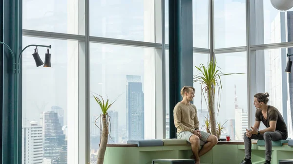 Two gentlemen have a meeting at a co working space on the top of a building with skyscrapers background. Two friends have conversation at an environmental friendly corner