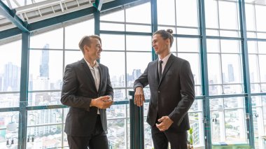 İki yönetici, şehir manzarası olan bir terasta yeni bir proje hakkında gayri resmi bir konuşma yapıyorlar. İş dünyası liderleri yeşil bir binada rahatlatıcı atmosfer altında fikir alışverişinde bulunurlar. Skylines arkaplanı