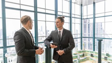 İki yönetici, şehir manzarası olan bir terasta yeni bir proje hakkında gayri resmi bir konuşma yapıyorlar. İş dünyası liderleri yeşil bir binada rahatlatıcı atmosfer altında fikir alışverişinde bulunurlar. Skylines arkaplanı
