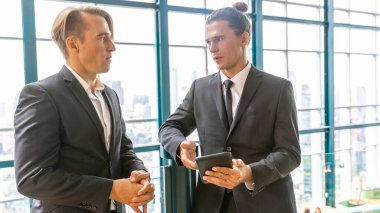 İki yönetici, şehir manzarası olan bir terasta yeni bir proje hakkında gayri resmi bir konuşma yapıyorlar. İş dünyası liderleri yeşil bir binada rahatlatıcı atmosfer altında fikir alışverişinde bulunurlar. Skylines arkaplanı