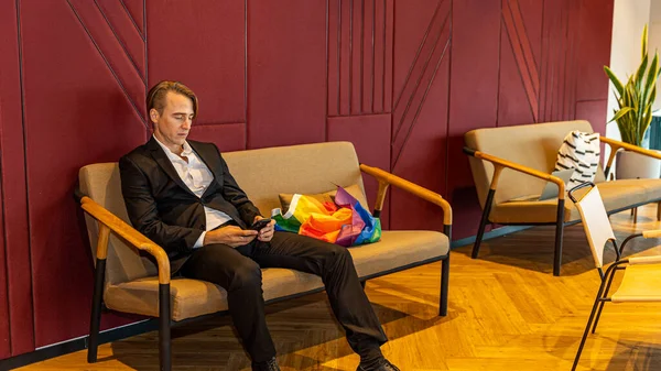 Young manager sits at an office lobby with LGBT flag on the chair. A male CEO uses LGBT flag to advocate for gender equality in an office. LGBT symbol in a business office for gender equity
