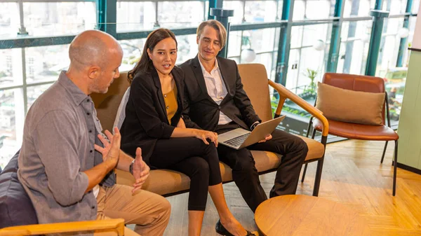 Investor is sharing his business view with managers in formal wear at a green terrace on a rooftop office with cityscape background. Group of managers from diverse cultures discuss with their boss