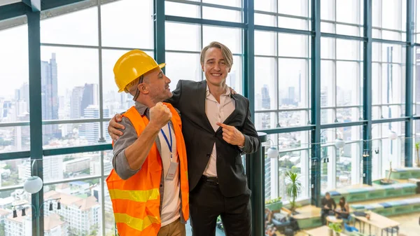 An investor under safety uniform and hard helmet set an agreement with his CEO for a new estate project on an office terrace with cityscape and skylines building background