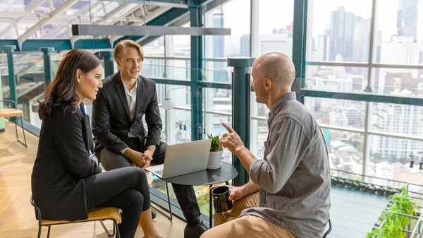 Investor is sharing his business view with managers in formal wear at a green terrace on a rooftop office with cityscape background. Group of managers from diverse cultures discuss with their boss