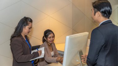 Resmi kıyafetlerle resepsiyonda ofis çalışanları arasında yapılan bir konuşma. Tezgahtaki ziyaretçi kaydını desteklemek için bilgisayar kullanıyor. Genç bayan memurun anahtar bilgileri