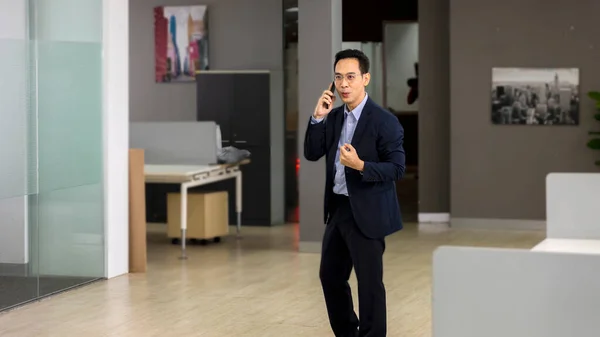 Male executive office with glasses has a phone call with colleague or client in an office. An Asian business man uses technology to connect and operate his project