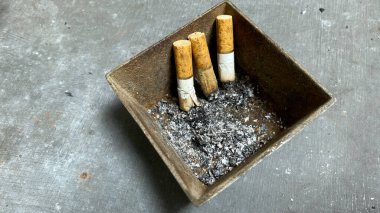 Kül tablası ve sigara izmaritleri gri masada.