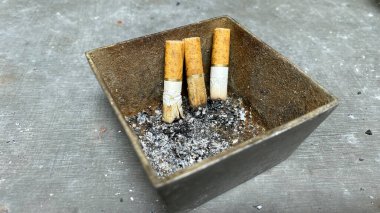 Kül tablası ve sigara izmaritleri gri masada.