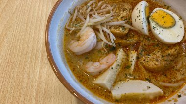 Bir kase laksa pirinçli şehriye, körili sos, haşlanmış fasulye filizi, soğan, tofu böreği ve balık köftesi.