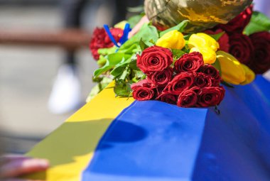 POLTAVA, UKRAINE - 24 Mart 2022 Ukrayna Silahlı Kuvvetleri 'nin şehit askerlerinin defin töreni sırasında Ukrayna bayrağıyla kaplanmış bir mezarda çiçek tutan bir asker