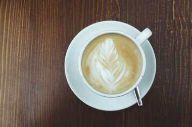 Gün boyunca tahta kahverengi bir masanın üzerinde bir fincan kahve var.