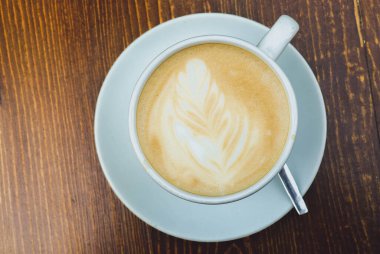 Gün boyunca tahta kahverengi bir masanın üzerinde bir fincan kahve var.