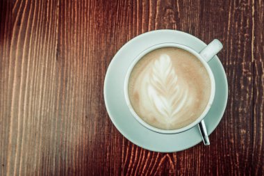 Gün boyunca tahta kahverengi bir masanın üzerinde bir fincan kahve var.