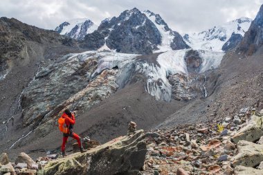 Uçurumun kenarında sırt çantalı bir fotoğrafçı. Tehlikeli dağlar ve uçurum. Mavi buzulun altındaki dağ vadisinin çarpıcı manzarası..