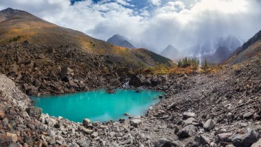 Sonbahar dağının panoramik manzarası, dağ yamaçlarının üzerindeki sis, dağ geçidini dolduran beyaz bulutlar. Açık mavi bir dağ gölü ve parlak bir sonbahar ormanı..