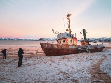 Photographers take photos of a ship washed up on the coast of the Arctic ocean by a storm. clipart