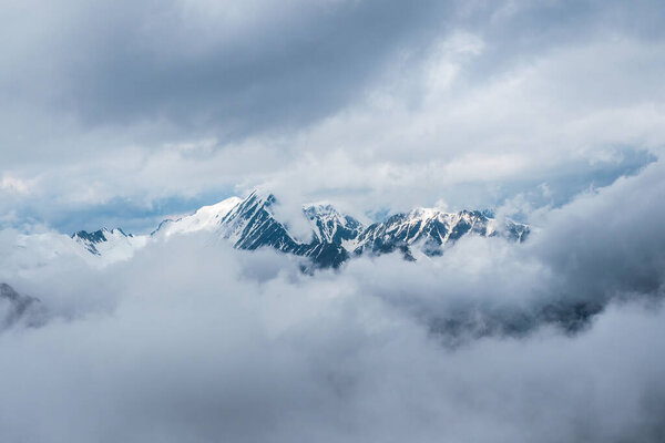 Soft focus. Wonderful minimalist landscape with big snowy mountain peaks above low clouds. Atmospheric minimalism with large snow mountain tops, dark glacier in dramatic sky.