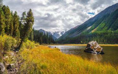 Gölün ortasında büyük bir granit taş var. Highland Valley 'de yüksek dağ boyunca güzel bir göl. Dağ gölünün taşlı durgun suları. Dağlık arazilerin sarı atmosferik doğal arkaplanı.