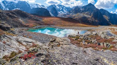 Yüksek irtifa vadisinde inanılmaz temiz bir dağ gölü. Altai dağlarının güzel doğası. Vadideki göl, kayalar ve kar. Muhteşem bulutlu, güneşli bir yaz günü. Panoramik görünüm.