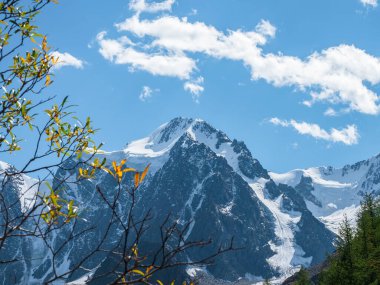Seçici odaklanma. Yüksek uçlu bir dağın tepesinde beyaz bulutlar. Karlı yüksek rakımlı dağ manzarası, karlı dağ zirvesi ve bulutlu mavi gökyüzünün altında keskin kayalar.. 