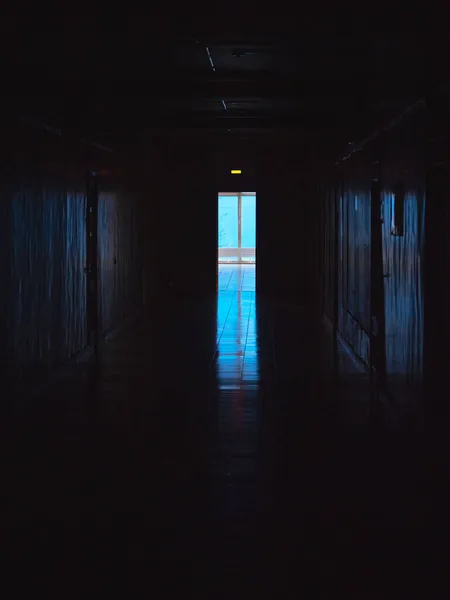 End of dark tunnel with magic blue light. Vertical view. Empty dark corridor in hospital laboratory. Blue light at the end of a dark corridor.