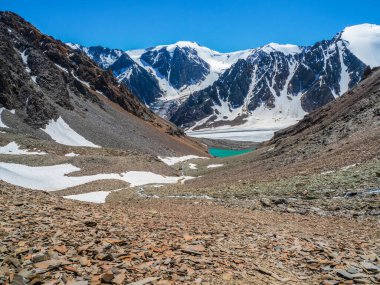 Caldera 'daki Mavi Dağ Gölü. Mavi bulutlu gökyüzüne karşı sıradağlar. Sönmüş bir volkanın Caldera 'sı bir dağ silsilesiyle çevrilidir. Vadide sarp kayalıkları olan mavi bir göl var.