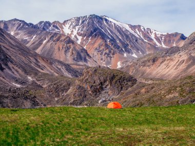 Tek başına yürüyüş. Yeşil kayalık yüksek rakımlı platoda kamp yapmak. Buzul ve yüksek karlı dağların arka planında turistik çadır.