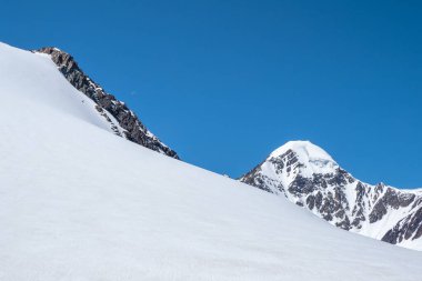 Kar bir dağ yamacında sürüklenir. Atmosferik dağ manzarası ve kayalık tepelerde buzullar. Güneş ışığında karlı taşlı geçitli muhteşem bir manzara..
