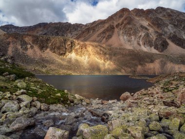 Yüksek dağlardaki parlak güneş ışığı. Dağların tepesindeki karanlık buzul gölü. Yüksek rakımlı vadide gölü olan atmosferik yeşil bir arazi..