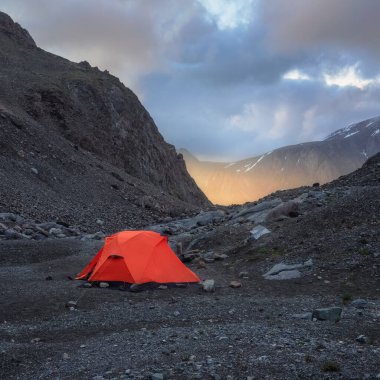 Gün doğumunda kayaların arasında kayalık tepede çadırlı sürrealist dağların kare manzarası. Alçak bulutlarda güzel sabah dağları. Dağlık bölgelerde, bulutlu havalarda çadırlı gerçeküstü bir manzara.. 
