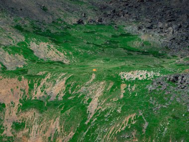 Büyük bir dağ yamacında küçük bir çadır. Seyahat ve macera romantizmi. Küçük bir çadırı olan yeşil bir dağ yamacının minimalist manzarası. Yeşil tepesinde çadırı olan yüksek manzaralı kayalar.