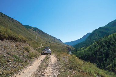 Toprak bir dağ yolunda kesişiyor. Taşların arasından araba geçiyor, dere yatağında dar yerlere gidiyor. Dağlarda uçsuz bucaksız bir yolculuk