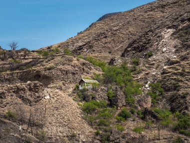 Ethnic house with garden at the edge of the abyss on a mountain peak at high altitude. A difficult life in a deep mountain gorge. Dagestan. 