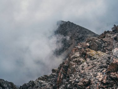Mountain view from cliff at high altitude. Mystical landscape with beautiful sharp rocks near precipice and couloirs in low clouds. Beautiful mountain foggy scenery on abyss edge with sharp stones.