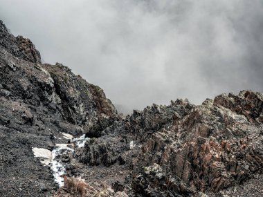Mountain view from cliff at high altitude. Mystical landscape with beautiful sharp rocks near precipice and couloirs in low clouds. Beautiful mountain foggy scenery on abyss edge with sharp stones.