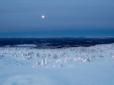Kuzey Rusya 'nın liman kenti Kandalaksha' nın uzak bir manzarasıyla kışın kutup tepesinin karla kaplı yamacında dolunay. Kış kutup manzarası. Soğuk kış havası. Sert kuzey iklimi