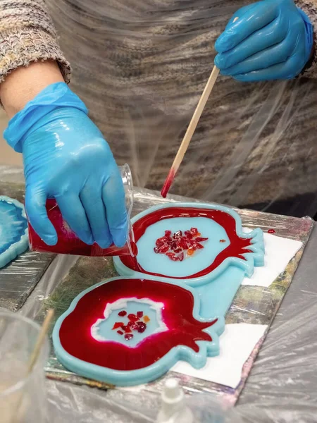 The art process of pouring epoxy resin into a wooden toy. Technology process of creating a painting in style resin art, works with epoxy in studio, makes a wooden stand with the image. Close up.
