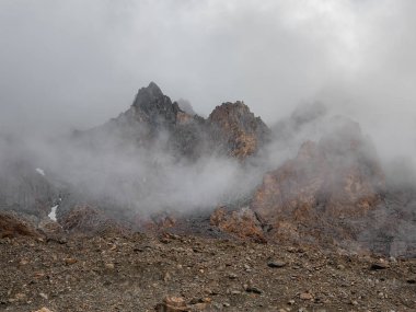 Soft focus. Atmospheric ghostly landscape with fuzzy silhouettes of sharp rocks in low clouds. Dramatic view to large mountains blurred in rain haze in gray low clouds.