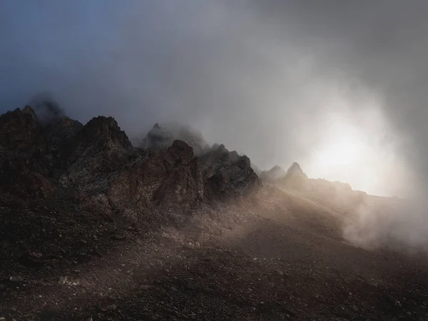 Soft focus. Darkness minimalist landscape with big mountain rocks above low clouds with sun rays. Atmospheric ghostly minimalism with large mountain tops in cloudy sky.