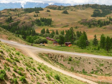 Picturesque summer mountain landscape with unpaved exit from the highway and road through the pass. Asphalt mountain highway. Chuysky trakt.  Empty highway through a high plateau. Campsite by the road