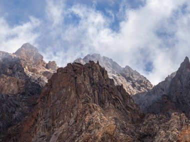 Scenic mountain landscape with sharp rocks under blue cloudy sky. Colorful scenery with foggy sharp rocky mountains. High rocky mountains in golden sunlight.