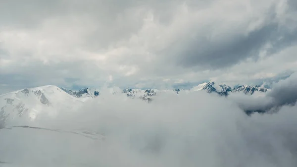 Soft focus. Wonderful minimalist landscape with big snowy mountain peaks above low clouds. Atmospheric minimalism with large snow mountain tops in cloudy sky. Panoramic view.