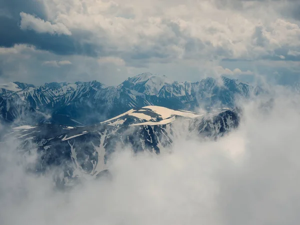 Soft focus. Wonderful minimalist landscape with big snowy mountain peaks above low clouds. Atmospheric minimalism with large snow mountain tops in cloudy sky.
