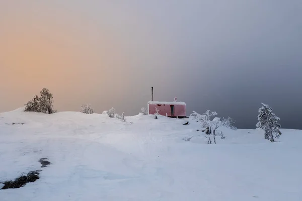 Cozy northern guest house on a snowy hill at dawn. Cabin in winter dawn.  Lonely house on a hilltop in the cool morning.