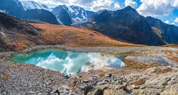 Amazing clean mountain lake in a high-altitude valley. Beautiful nature of Altai mountains. Lake in the valley, rocks and snow. Wonderful summer sunny day with gorgeous cloudscape. Panoramic view.