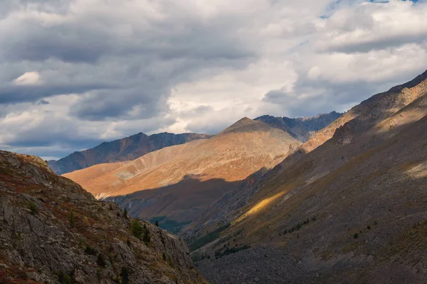 Dramatic foggy landscape with sunlit sharp mountain ridge under low clouds in sunset colors at changeable weather. Atmospheric mountain scenery with large sharp rocks on ridge top under cloudy sky.