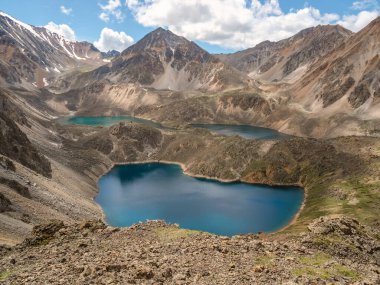 Bright summer group of azure and turquoise mountain lakes at various heights among black rocks. Three blue alpine lakes at different highs among sunlit black green rocky hills in highlands.